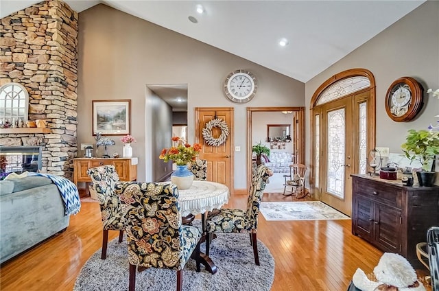 dining space with a stone fireplace, light wood-style flooring, french doors, and high vaulted ceiling