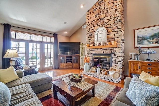 living room featuring a stone fireplace, wood finished floors, visible vents, and high vaulted ceiling