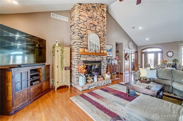 living room with visible vents, light wood-style flooring, a stone fireplace, and high vaulted ceiling