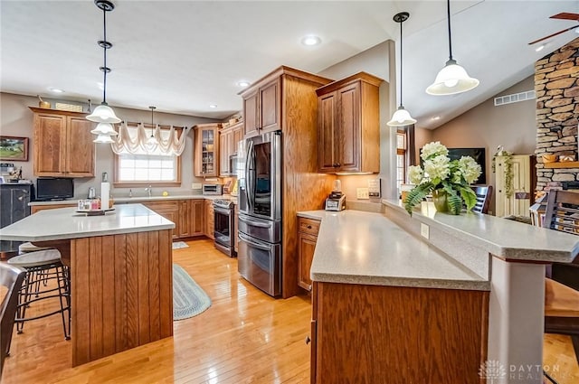 kitchen featuring visible vents, brown cabinets, a kitchen breakfast bar, light wood-style flooring, and stainless steel appliances