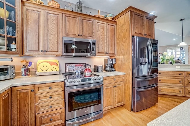 kitchen with light wood finished floors, appliances with stainless steel finishes, glass insert cabinets, and light countertops