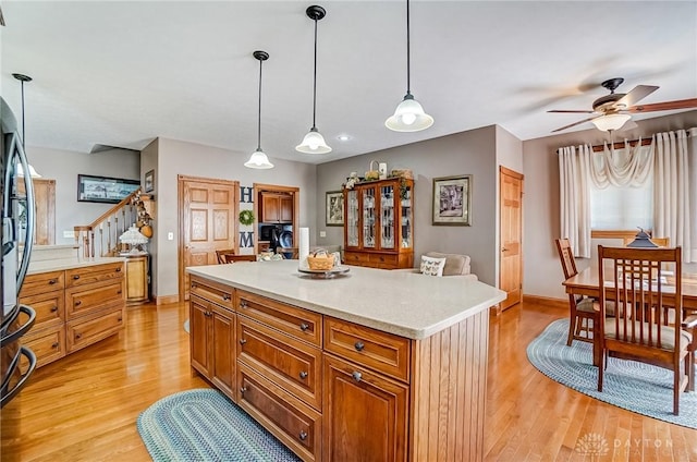 kitchen with brown cabinetry, light wood-style flooring, pendant lighting, and light countertops