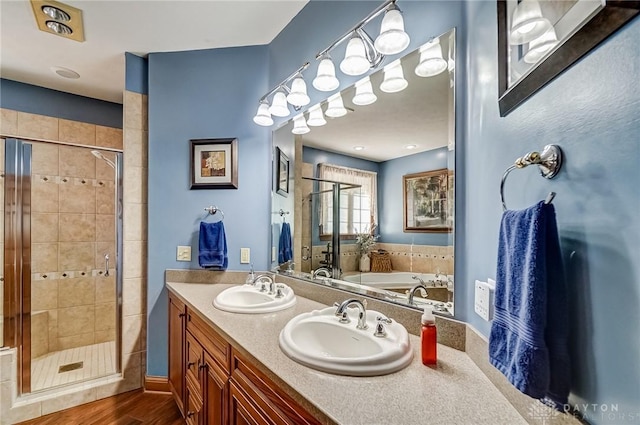 bathroom featuring a sink, wood finished floors, a stall shower, and double vanity