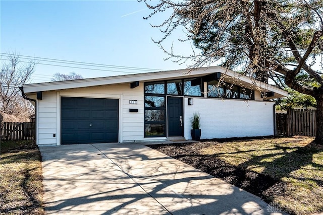 mid-century home with brick siding, an attached garage, concrete driveway, and fence