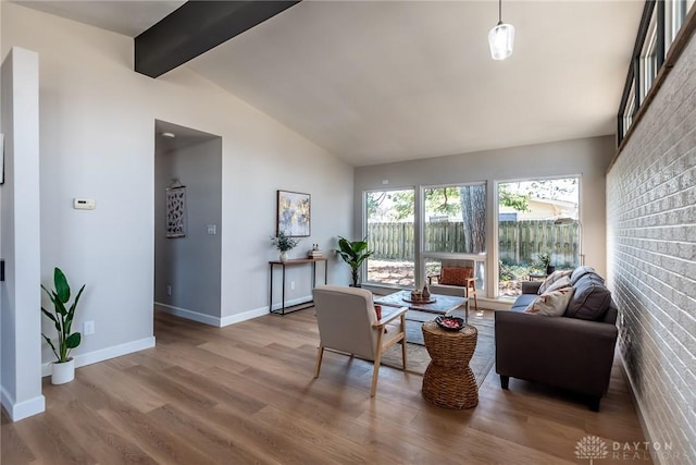 living room with baseboards, brick wall, wood finished floors, and vaulted ceiling with beams