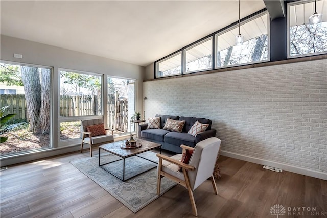 living area with brick wall, high vaulted ceiling, baseboards, and wood finished floors