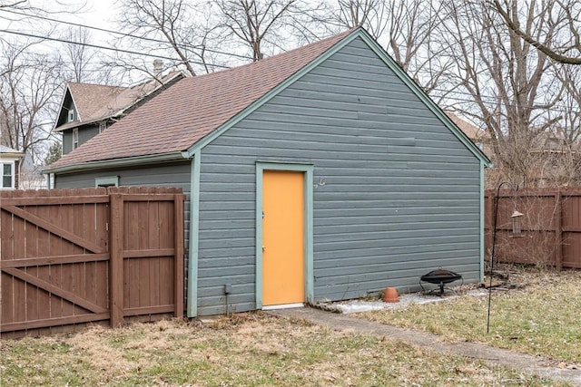 rear view of property featuring roof with shingles, an outdoor structure, and fence