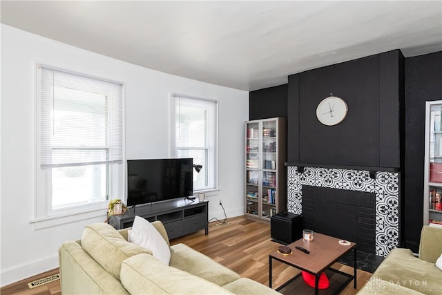 living area featuring wood finished floors, a healthy amount of sunlight, visible vents, and a tile fireplace