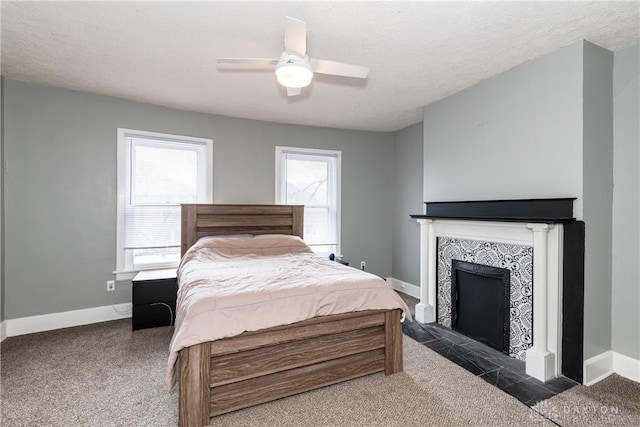 bedroom featuring a ceiling fan, baseboards, a textured ceiling, a tiled fireplace, and dark carpet