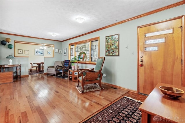 living room with ceiling fan, baseboards, ornamental molding, a textured ceiling, and wood-type flooring