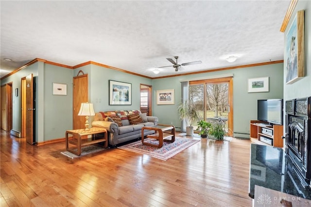 living area with baseboards, baseboard heating, light wood-style floors, a textured ceiling, and a ceiling fan