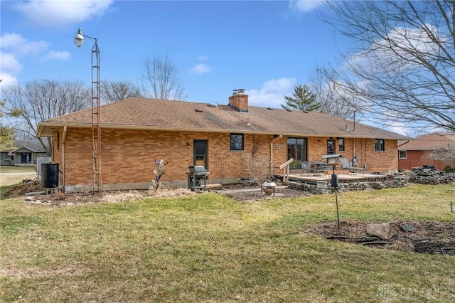 back of property featuring a lawn, brick siding, roof with shingles, and a chimney