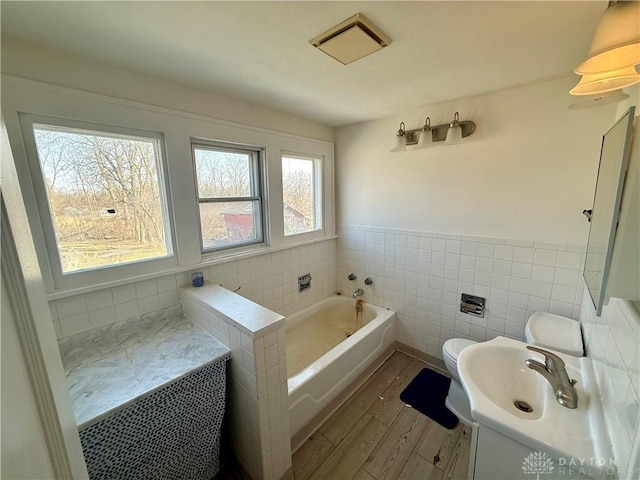 full bath with a wainscoted wall, vanity, wood finished floors, a bath, and tile walls