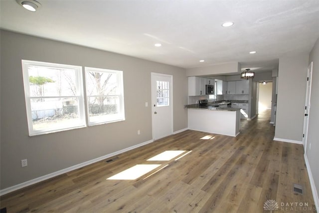 kitchen featuring baseboards, dark wood finished floors, a peninsula, recessed lighting, and dark countertops