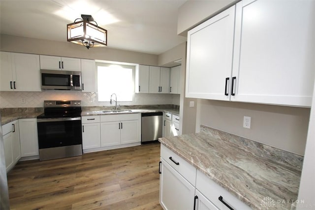 kitchen with light stone countertops, a sink, stainless steel appliances, white cabinets, and light wood-type flooring