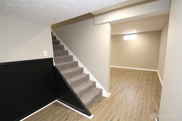 staircase with a textured ceiling, baseboards, and wood finished floors