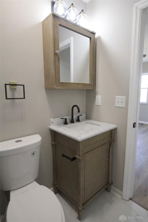 bathroom with toilet, vanity, marble finish floor, and baseboards