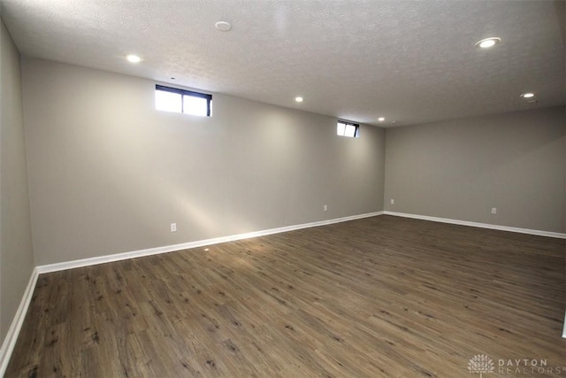 below grade area featuring recessed lighting, a textured ceiling, baseboards, and dark wood-style flooring