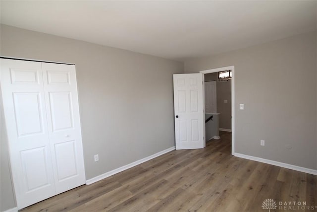 unfurnished bedroom featuring wood finished floors, baseboards, and a closet