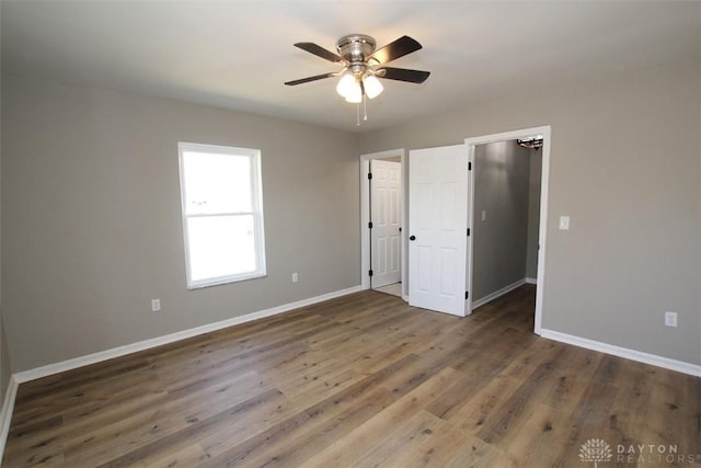 unfurnished bedroom featuring ceiling fan, baseboards, wood finished floors, and a spacious closet