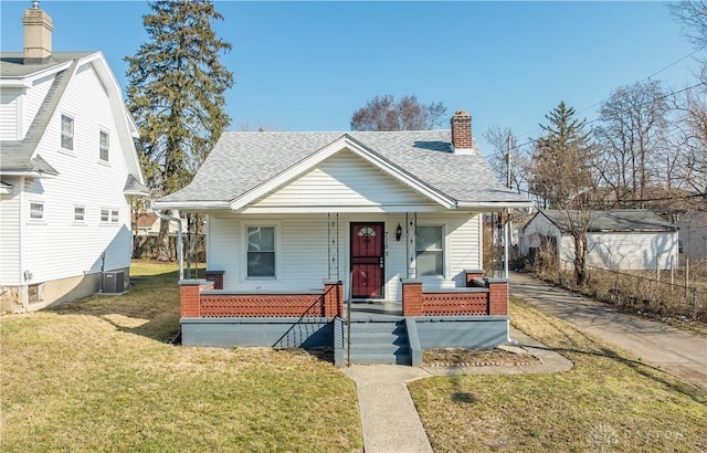 bungalow with cooling unit, roof with shingles, a porch, a chimney, and a front lawn