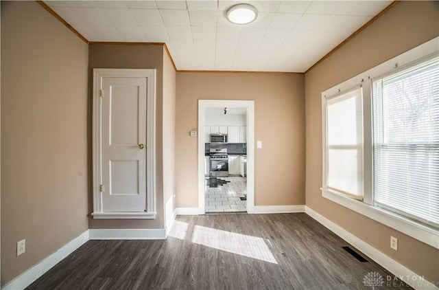 unfurnished room featuring visible vents, baseboards, crown molding, and dark wood-type flooring