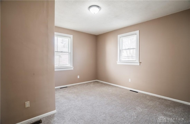 carpeted empty room featuring a wealth of natural light, visible vents, and baseboards