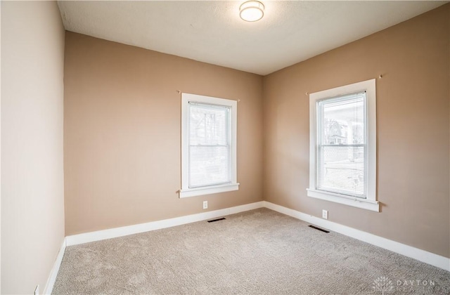 carpeted spare room with a wealth of natural light, visible vents, and baseboards