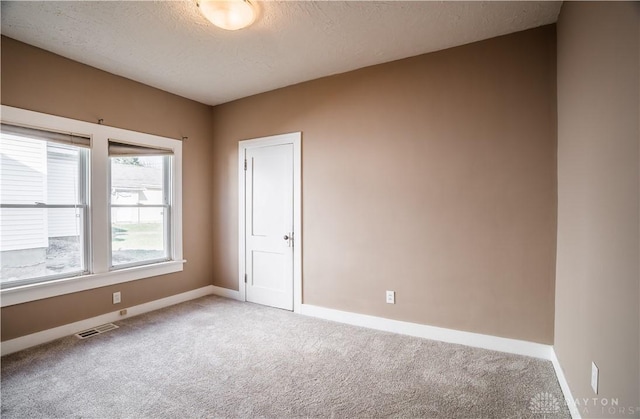 carpeted spare room featuring baseboards, visible vents, and a textured ceiling