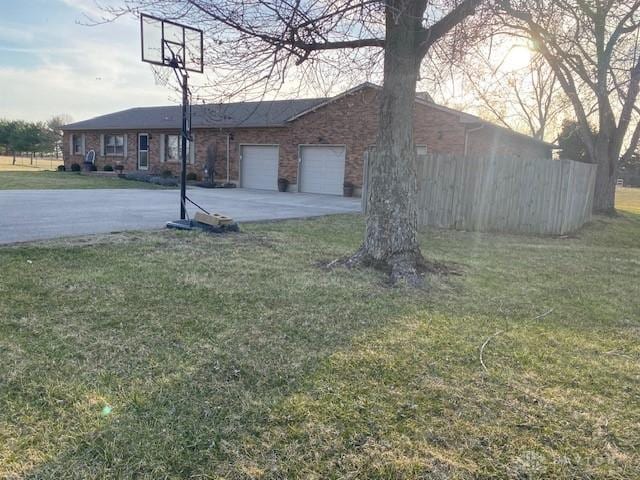 view of yard with an attached garage, driveway, and fence