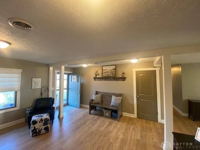 living area featuring a textured ceiling, baseboards, visible vents, and light wood-type flooring