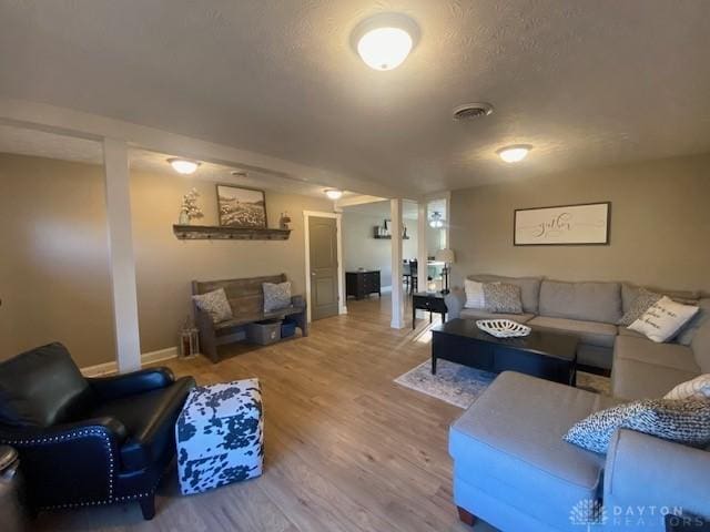 living area featuring visible vents, a textured ceiling, baseboards, and wood finished floors