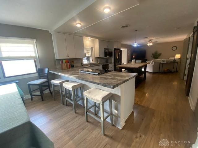 kitchen featuring a peninsula, white cabinets, black refrigerator, stainless steel microwave, and light wood-type flooring