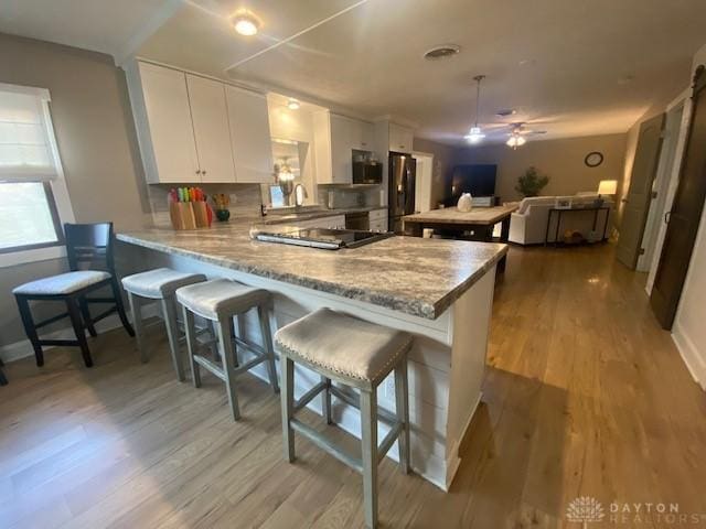 kitchen featuring white cabinets, a peninsula, stainless steel appliances, and light wood-type flooring