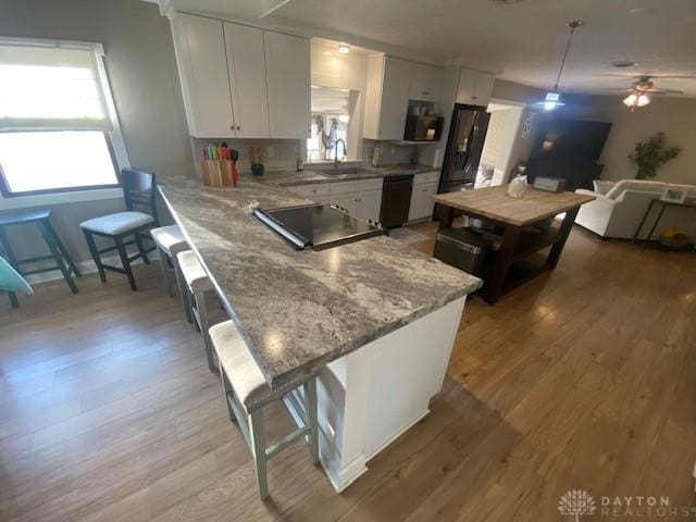 kitchen featuring light wood finished floors, dishwasher, a breakfast bar, white cabinets, and a sink