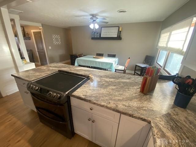 kitchen featuring electric range, light stone counters, wood finished floors, white cabinetry, and ceiling fan