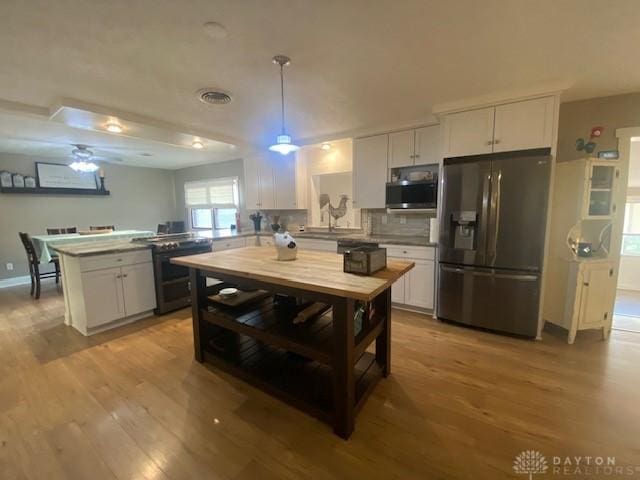 kitchen with white cabinetry, a peninsula, stainless steel appliances, and wood finished floors