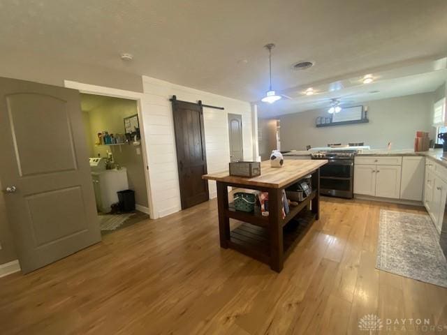 kitchen featuring light wood-style flooring, range with two ovens, light countertops, white cabinetry, and a barn door