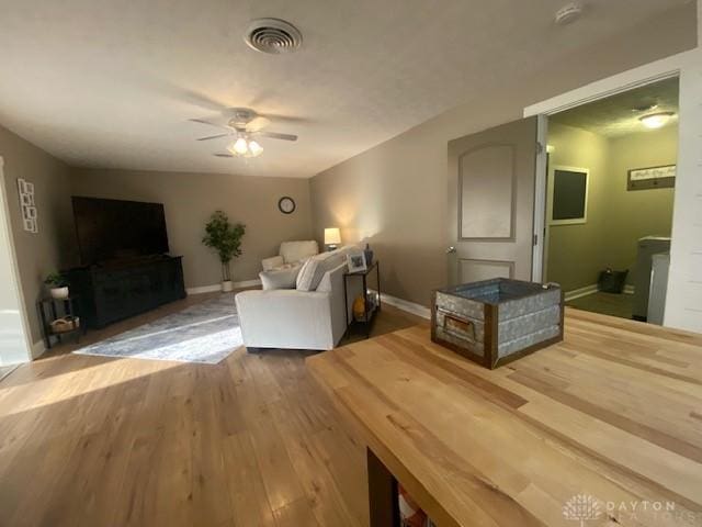 living area with ceiling fan, wood finished floors, visible vents, and baseboards