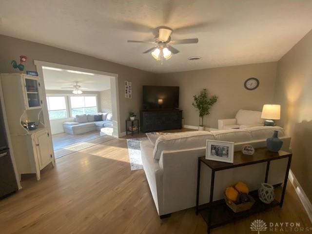 living room featuring a ceiling fan, baseboards, and wood finished floors