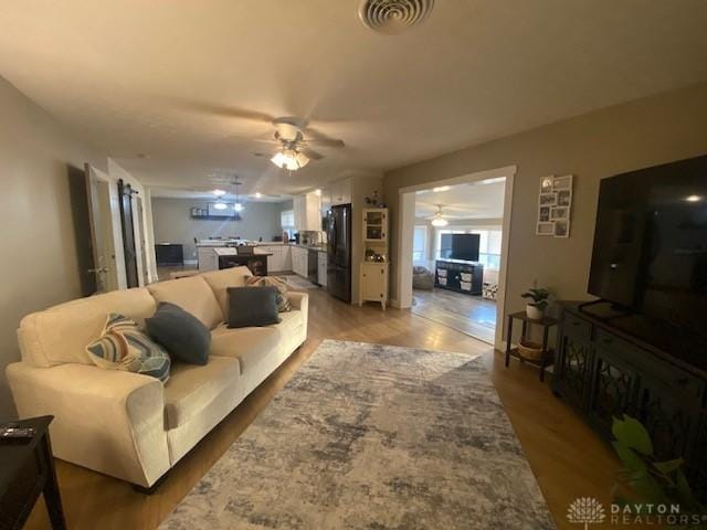 living room with light wood-style flooring, a ceiling fan, and visible vents