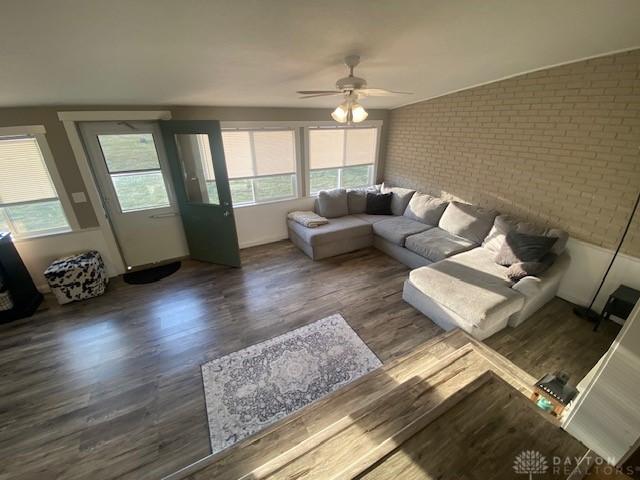 living room with wood finished floors, brick wall, and ceiling fan