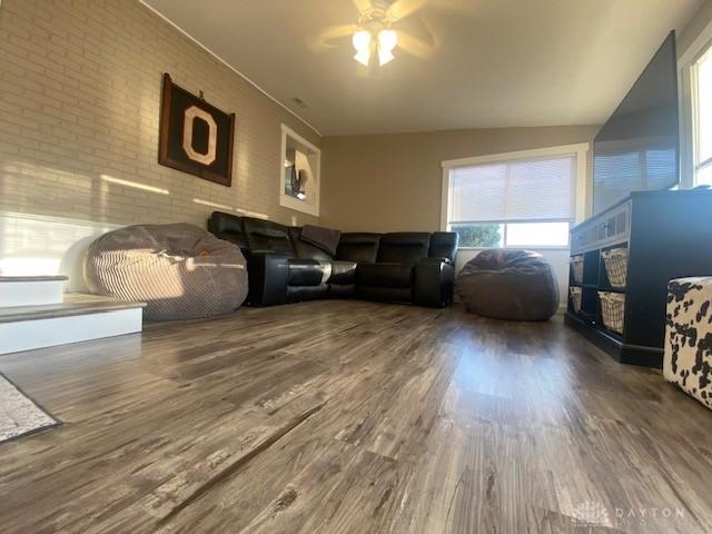 living room with ceiling fan, wood finished floors, and brick wall