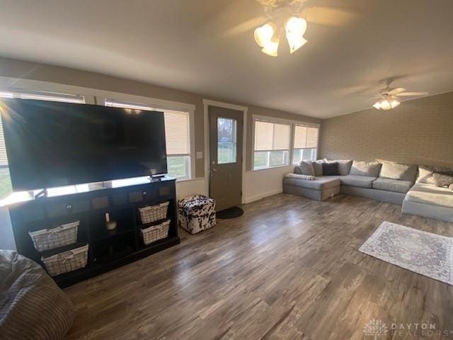 living room featuring a ceiling fan, wood finished floors, brick wall, and a healthy amount of sunlight