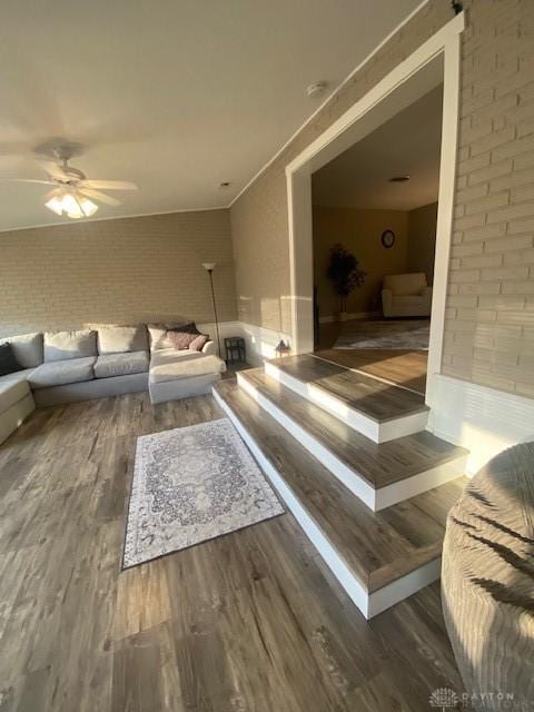 living room featuring wood finished floors, brick wall, and ceiling fan