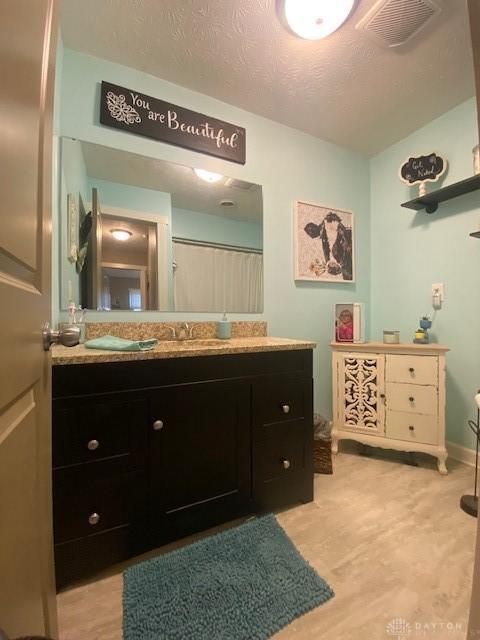 full bath with visible vents, a textured ceiling, vanity, and wood finished floors