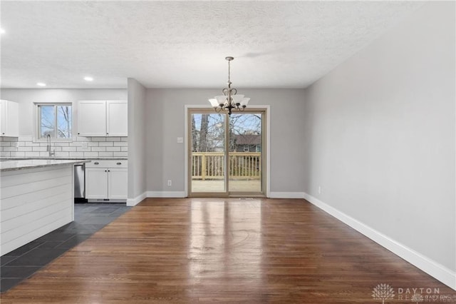 unfurnished dining area with baseboards, a notable chandelier, dark wood-style flooring, and a textured ceiling