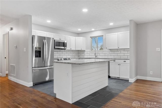 kitchen featuring decorative backsplash, white cabinets, appliances with stainless steel finishes, and a kitchen island