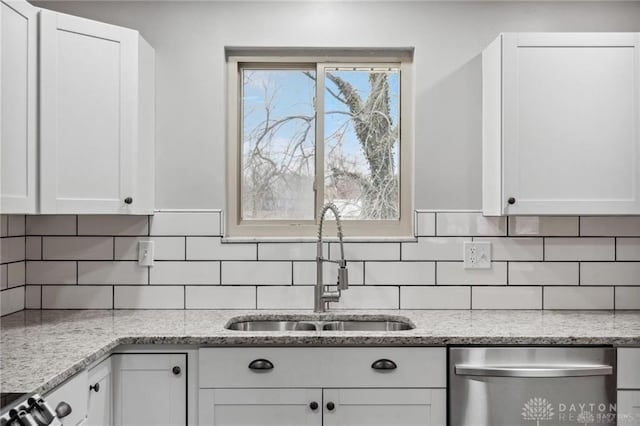 kitchen featuring light stone counters, dishwasher, white cabinetry, and a sink