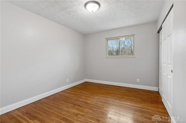 unfurnished bedroom with a closet, a textured ceiling, baseboards, and wood finished floors